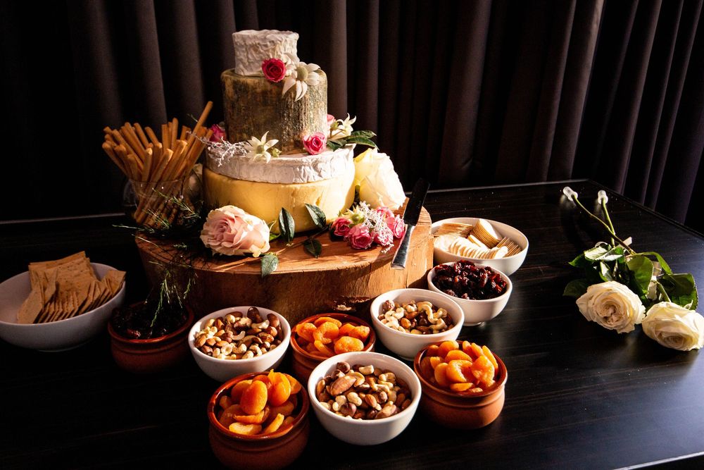 Elegant wedding dessert and snack table with tiered cake and various appetizers on dark tablecloth.