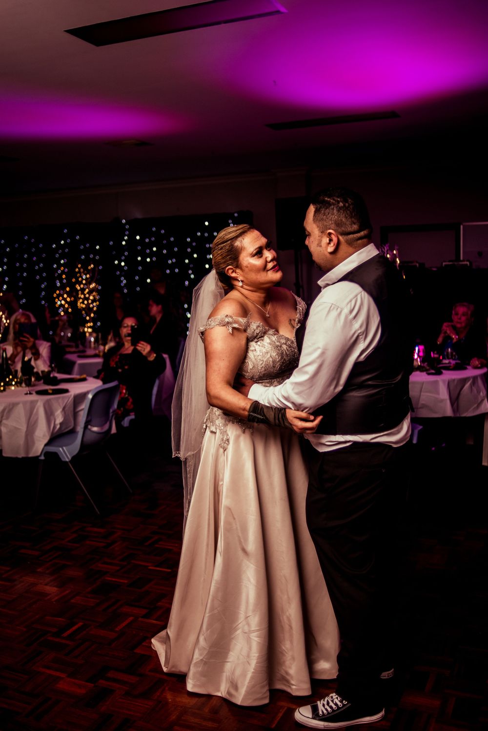 A couple shares their first dance under purple lighting at their wedding reception.