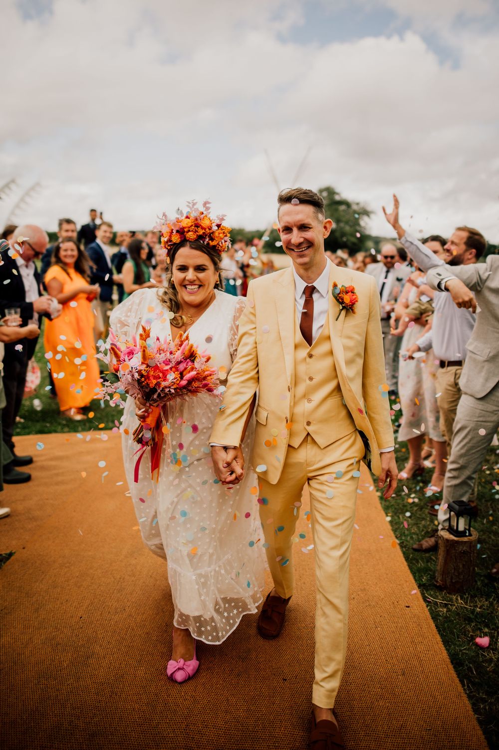 Wedding celebration on a dirt path with guests cheering and coral flower decorations. Worcestershire Wedding photographer.
