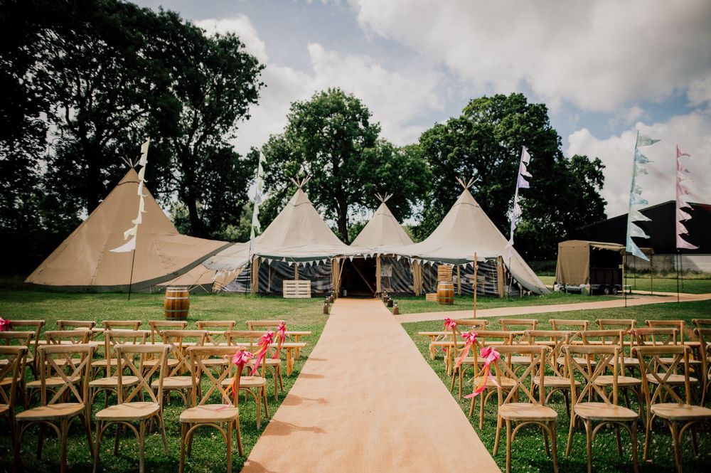 Outdoor wedding ceremony setup with white tipi tents and wooden chairs. Worcestershire Wedding photographer.