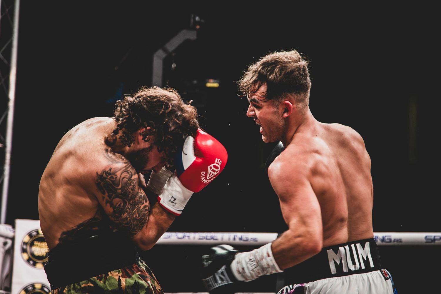 Two boxers in intense combat during professional match, one in green shorts, other in gold.