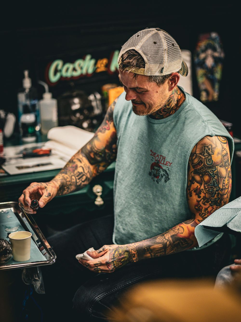 Tattooed person in teal shirt using digital device at counter.