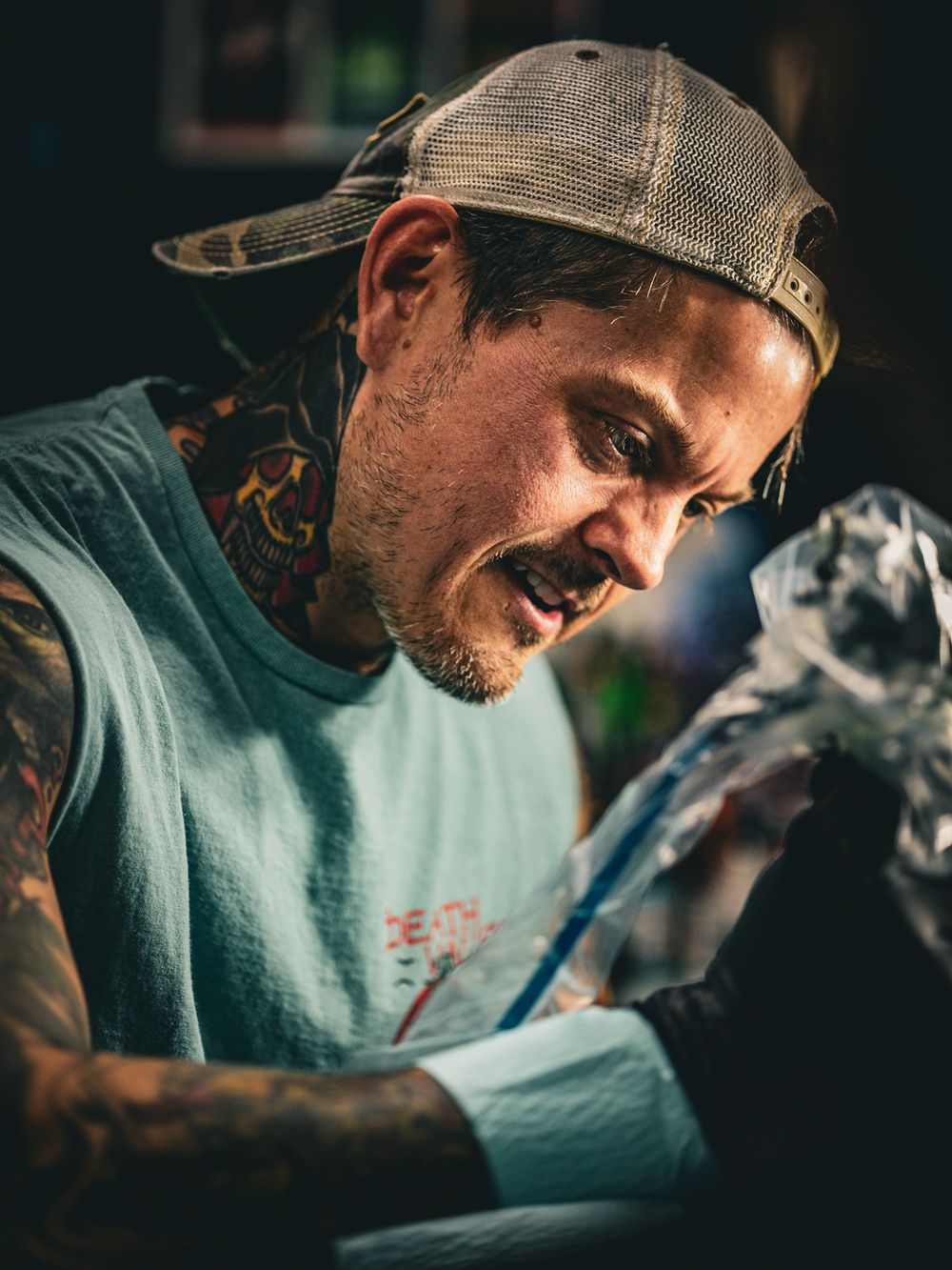 Individual in baseball cap and teal shirt working in low-light setting.