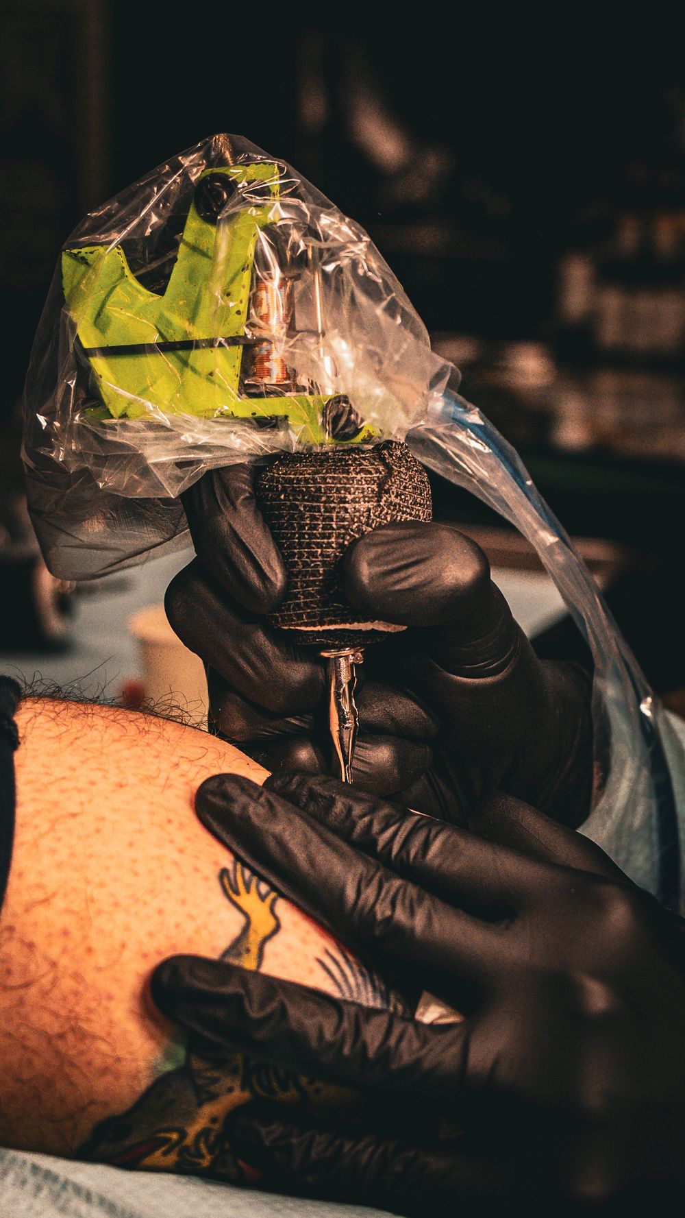 Tattoo artist wearing black gloves prepares equipment for a session in dark studio lighting.