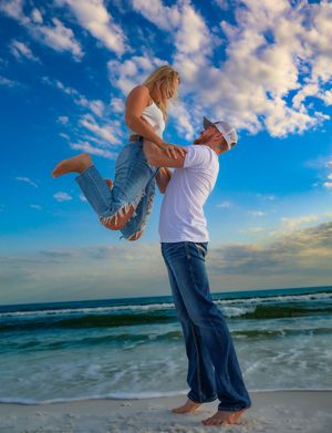 A playful beach photoshoot featuring a lift pose against a vibrant blue sky with ocean waves.