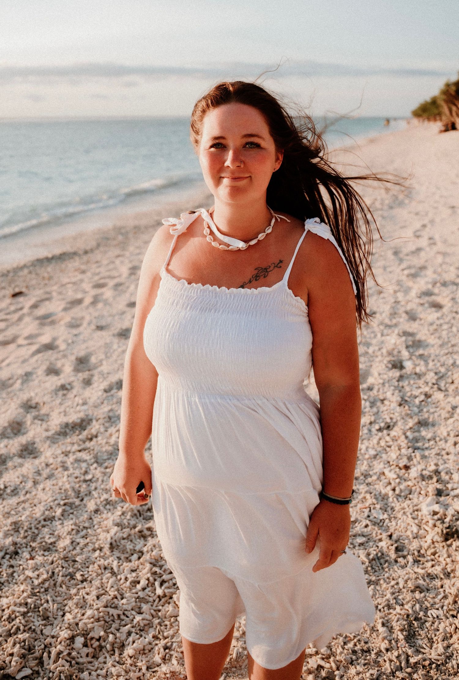 A beachside portrait in white summer dress with wind-swept hair during golden hour.