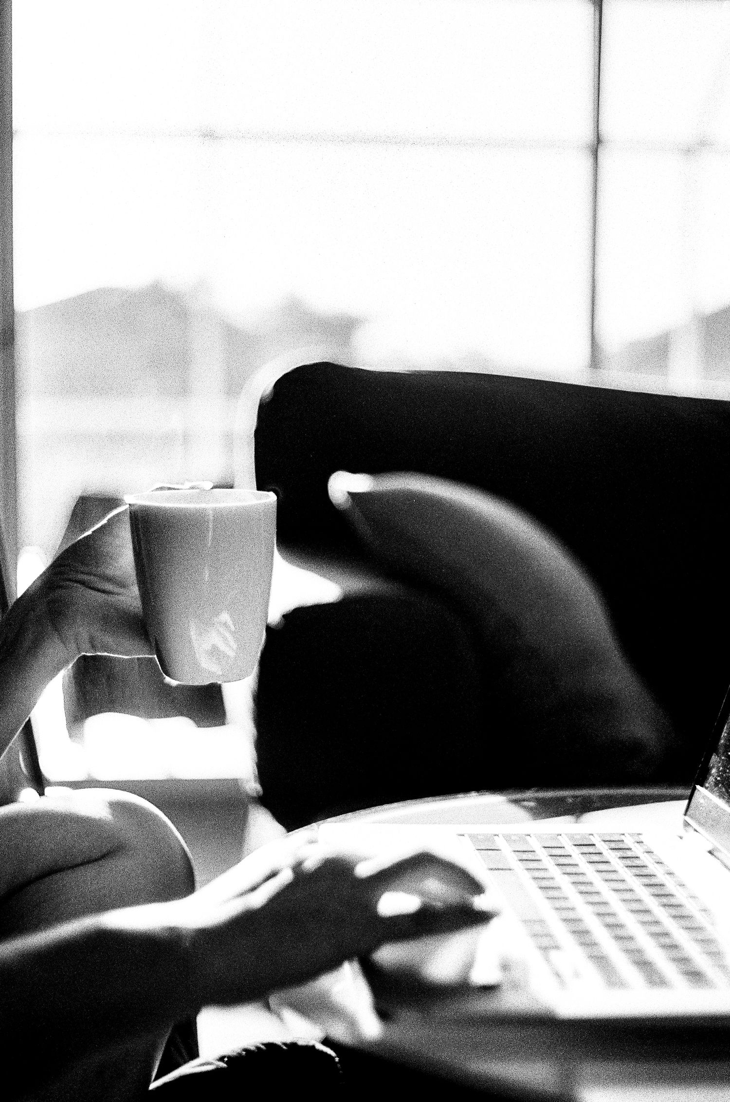 Black and white image of a laptop computer and coffee cup in a cozy indoor setting.