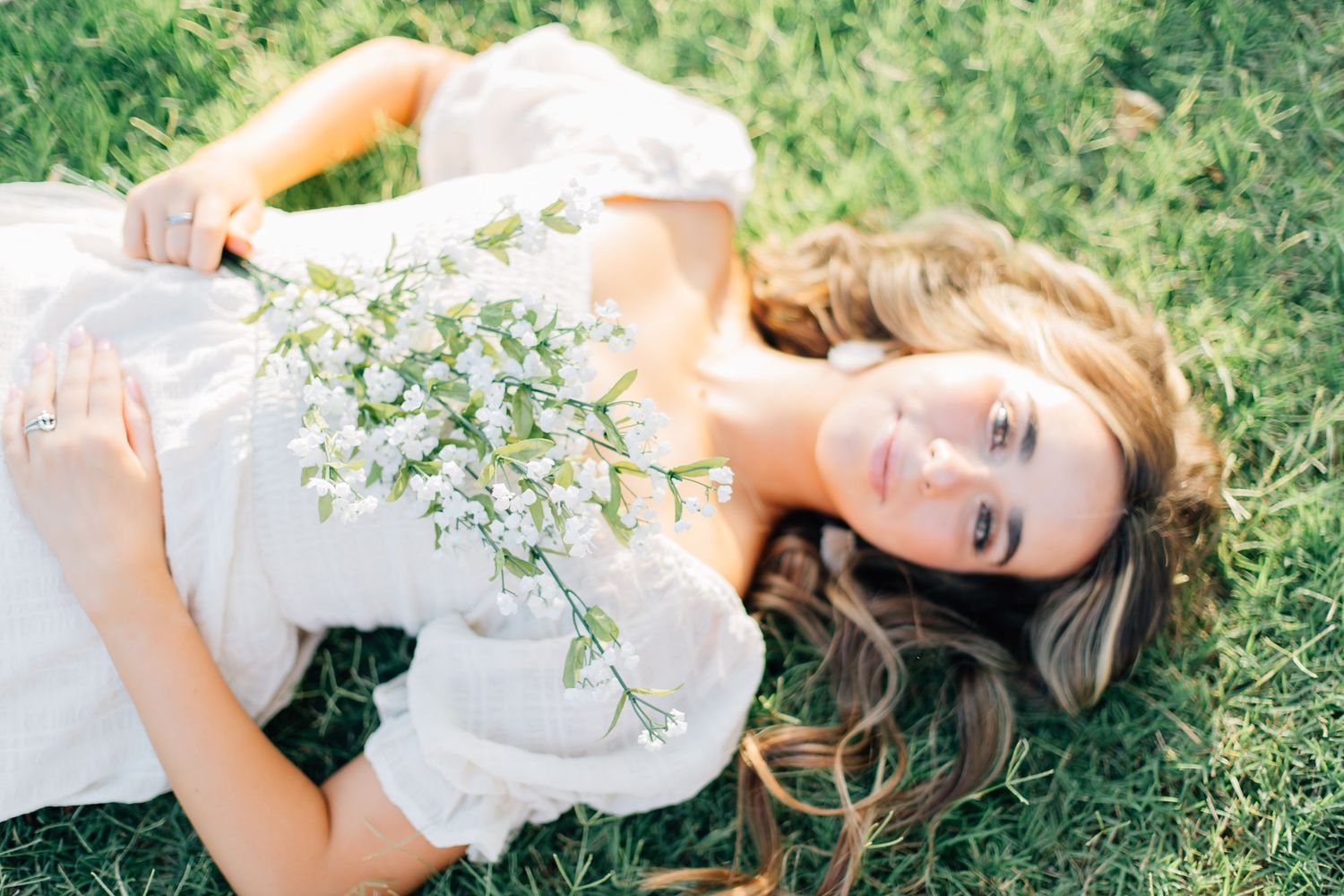 Woman in white dress lying on grass holding delicate white flowers.