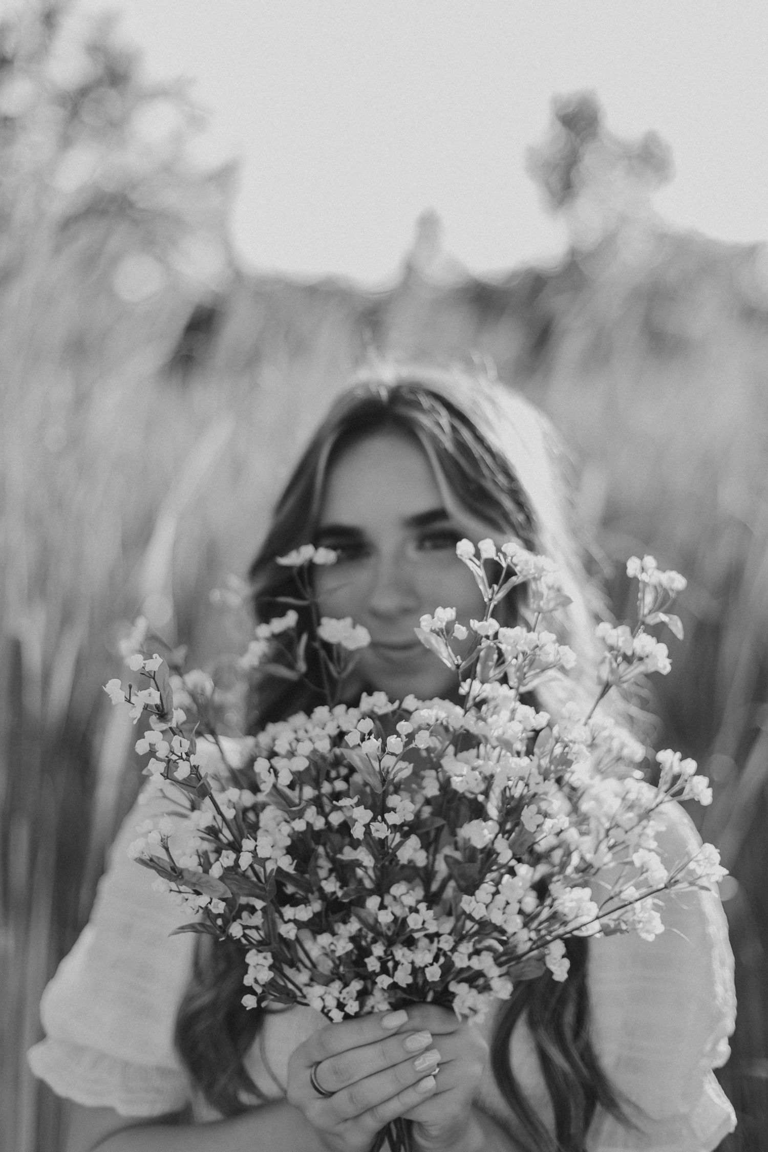 Black and white portrait of woman holding flowers in front of her face.