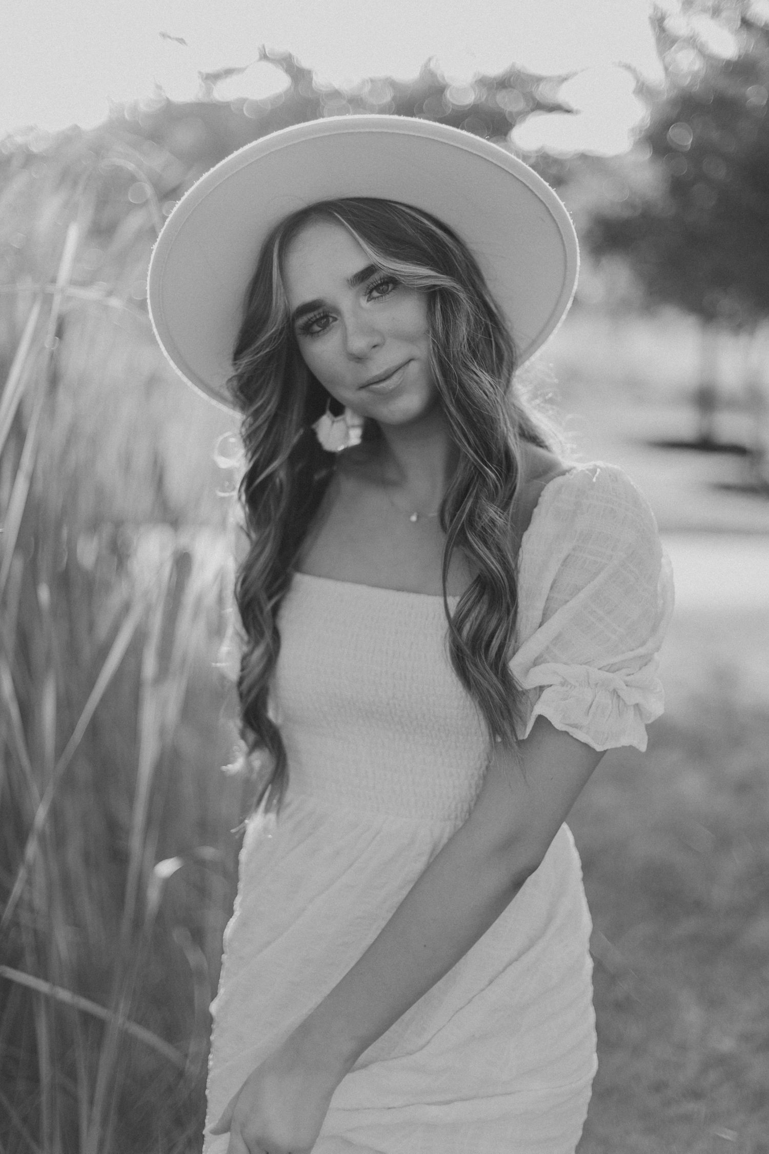 Black and white portrait of a woman in a white dress and hat with cattails in the background.
