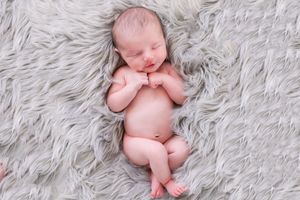 Peaceful sleeping newborn baby curled up on a soft white fluffy fur blanket.