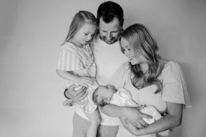 Black and white family portrait of parents with toddler girl and newborn baby in mothers arms.