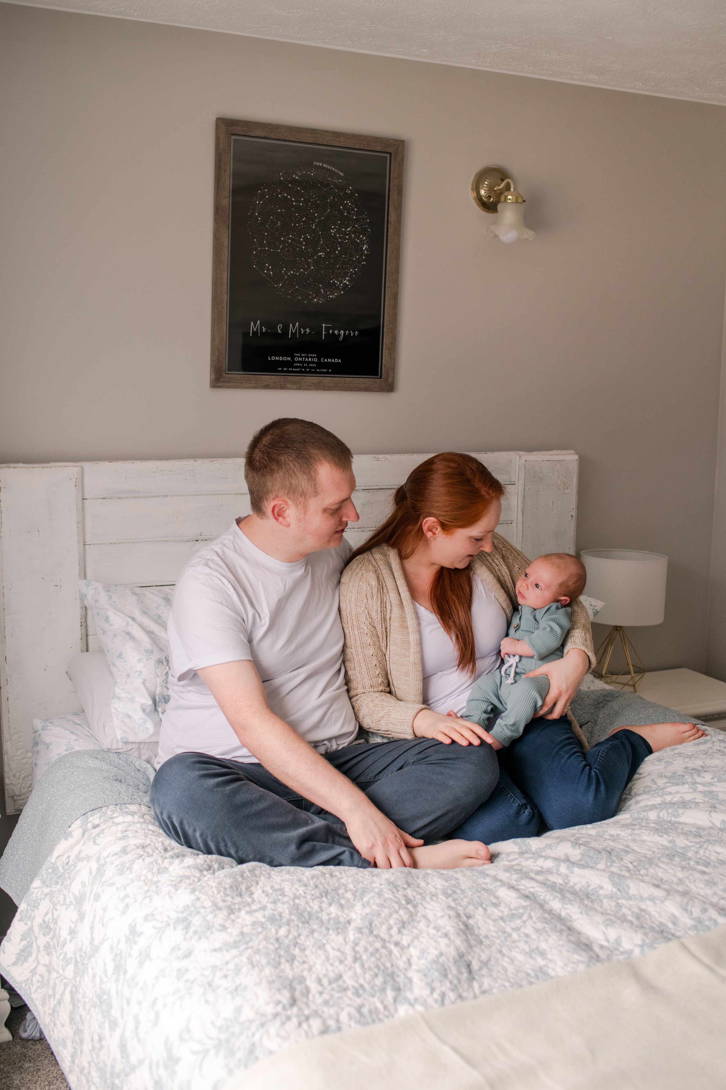 Young family sitting on bed admiring their newborn baby in cozy bedroom setting.