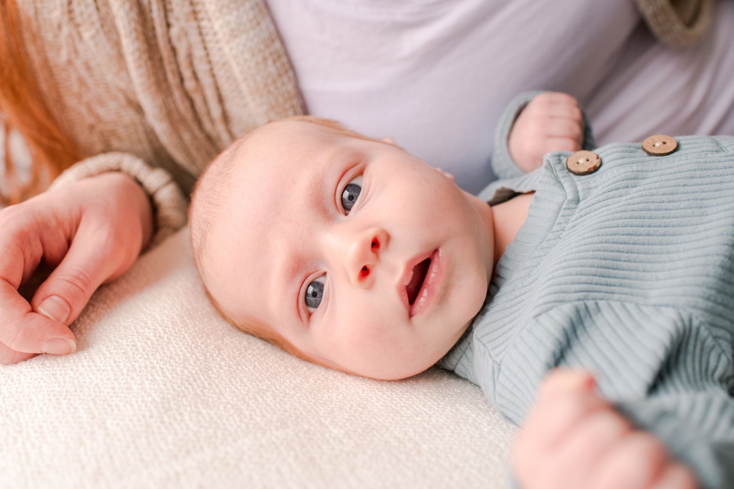 Adorable newborn baby with blue eyes lying on white blanket in sage green onesie.