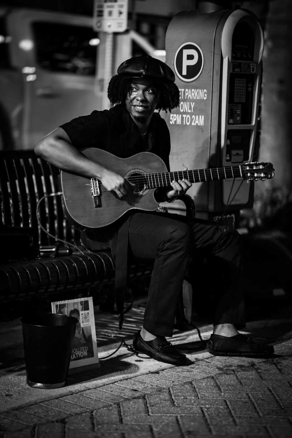 Black and white photograph of a street musician playing acoustic guitar at night.
