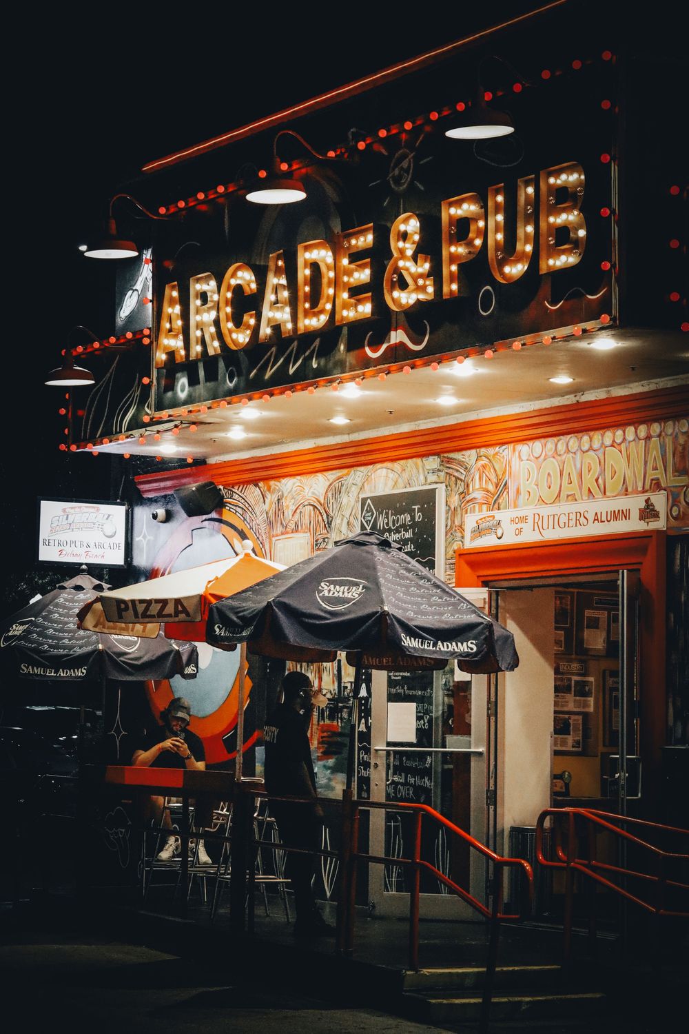 Illuminated arcade storefront with neon signs and umbrellas at night.