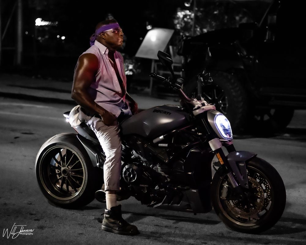 Motorcycles lined up at night with selective color highlighting pink details.