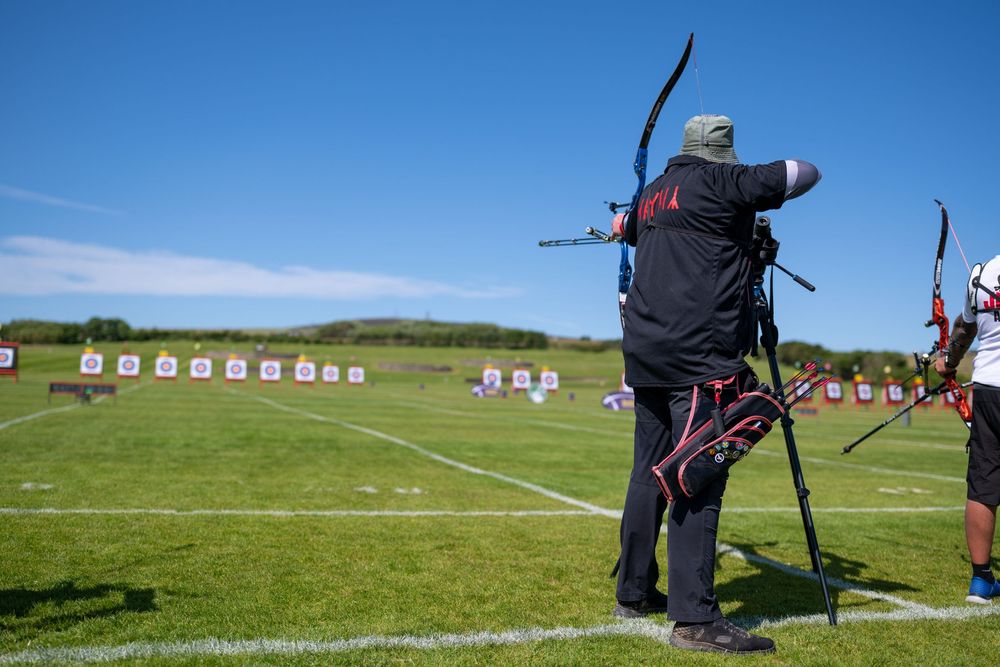 Archers practicing at an outdoor archery range with targets lined up in the distance on a sunny day.
