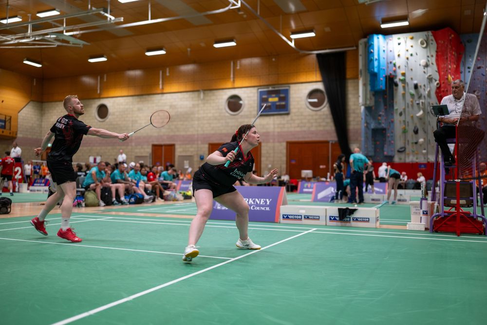 Indoor badminton players compete on a green court during a tournament match.