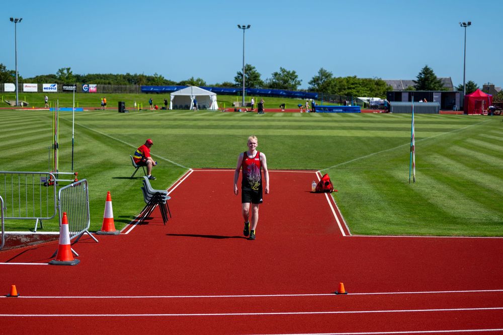 Athletes training on a red running track and green sports field under bright sunny conditions.