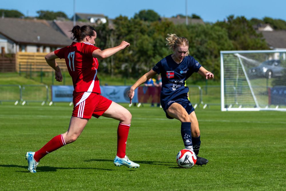 Soccer players compete for possession of the ball during an intense match on a sunny grass field.