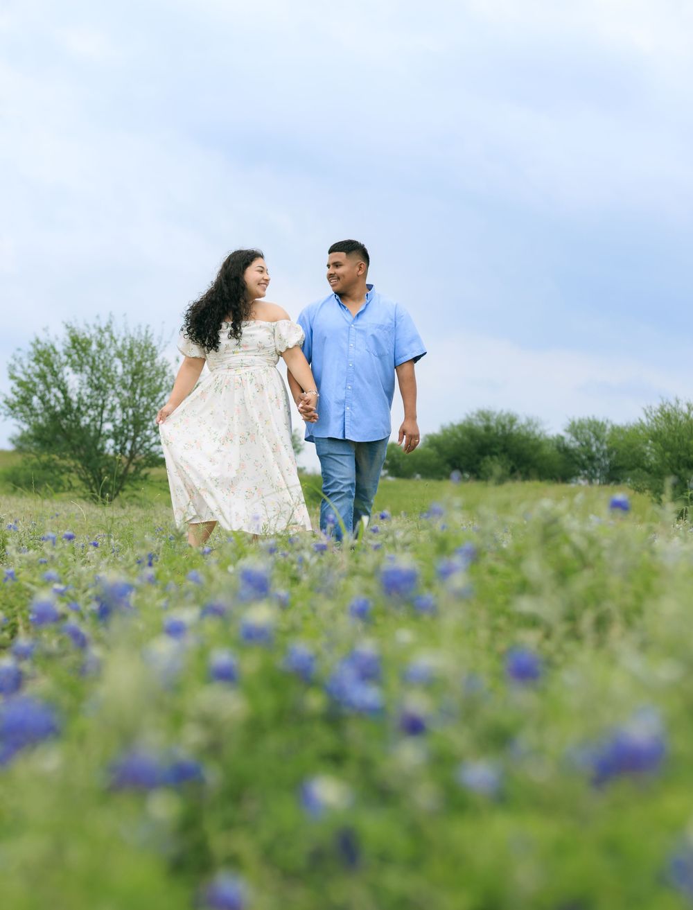 Couple portrait session in a blue bonnet field holding hands and mesmerizing into each other's eyes.