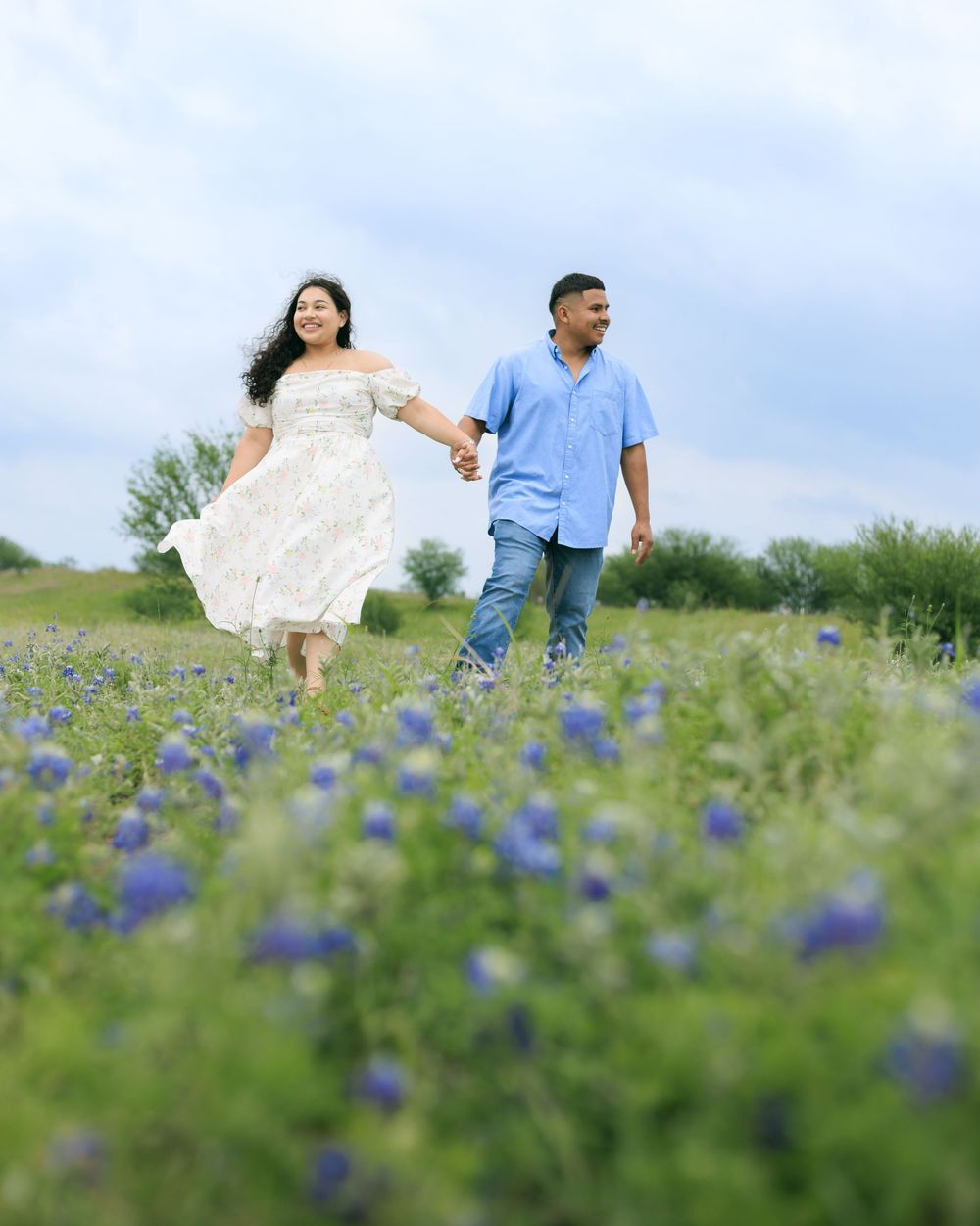Couple session in a blue bonnet field walking through the field holding hands.