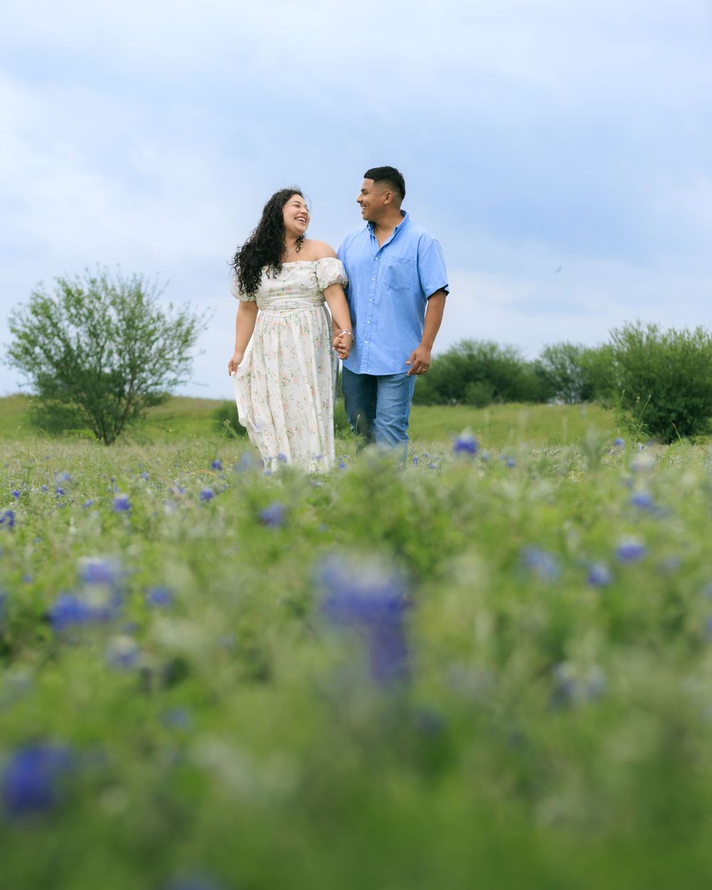 Couple portrait session in a blue bonnet field holding hands and mesmerizing into each other's eyes.