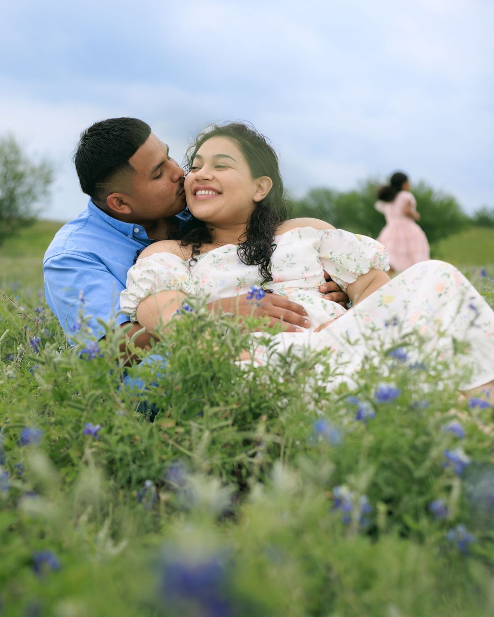 Couple session in blue bonnet field while husband kisses wife on the cheek.