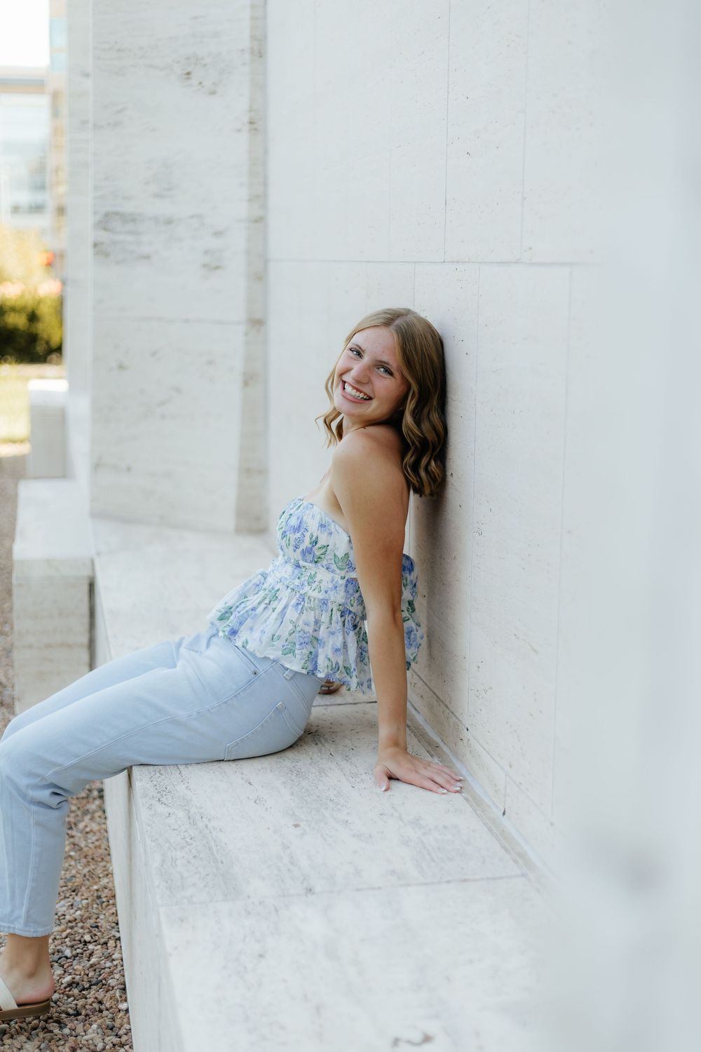 A person in a light blue dress poses gracefully against a white stone wall in an artistic outdoor photoshoot.
