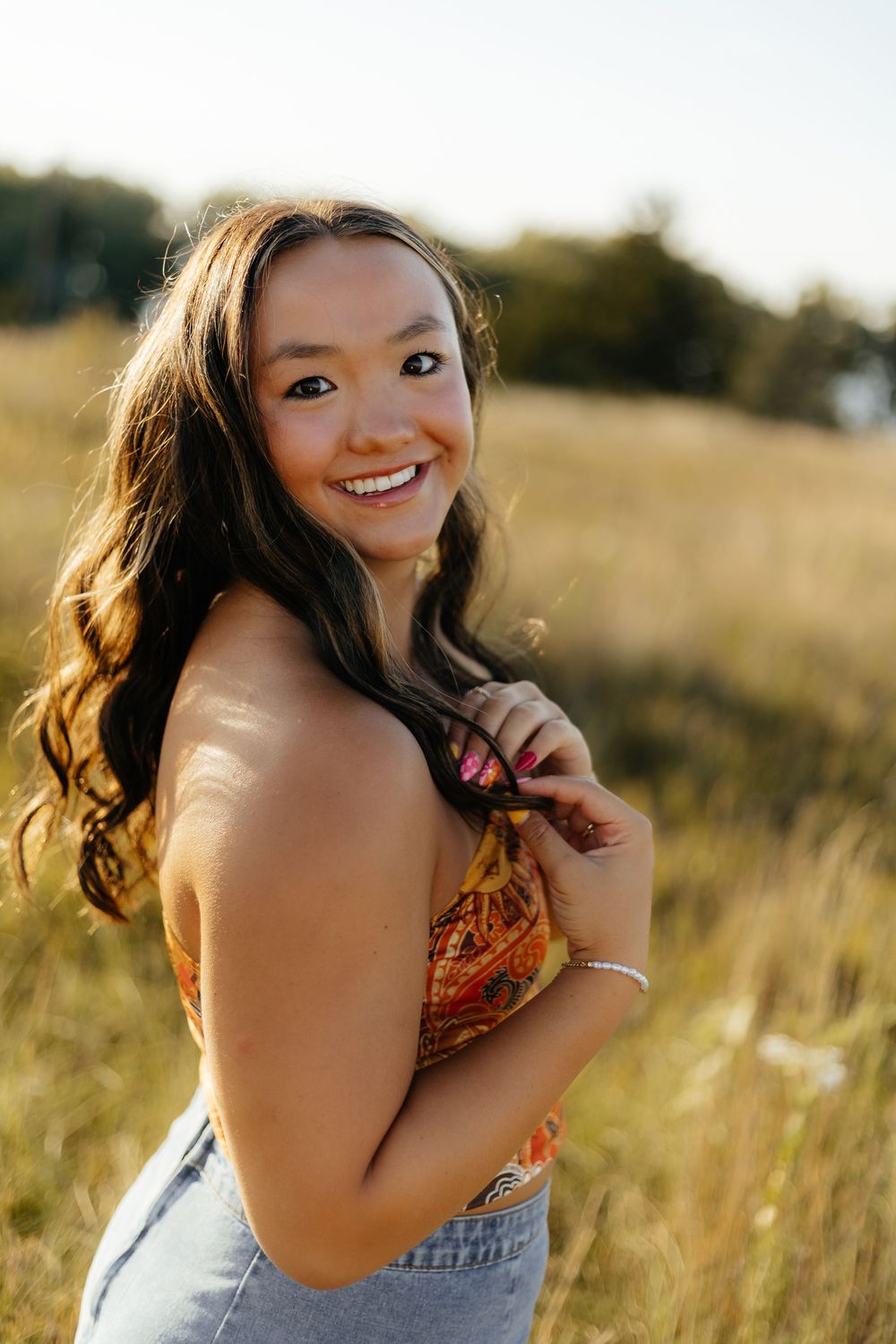 A joyful portrait in a golden field at sunset with warm lighting and a casual summer outfit.