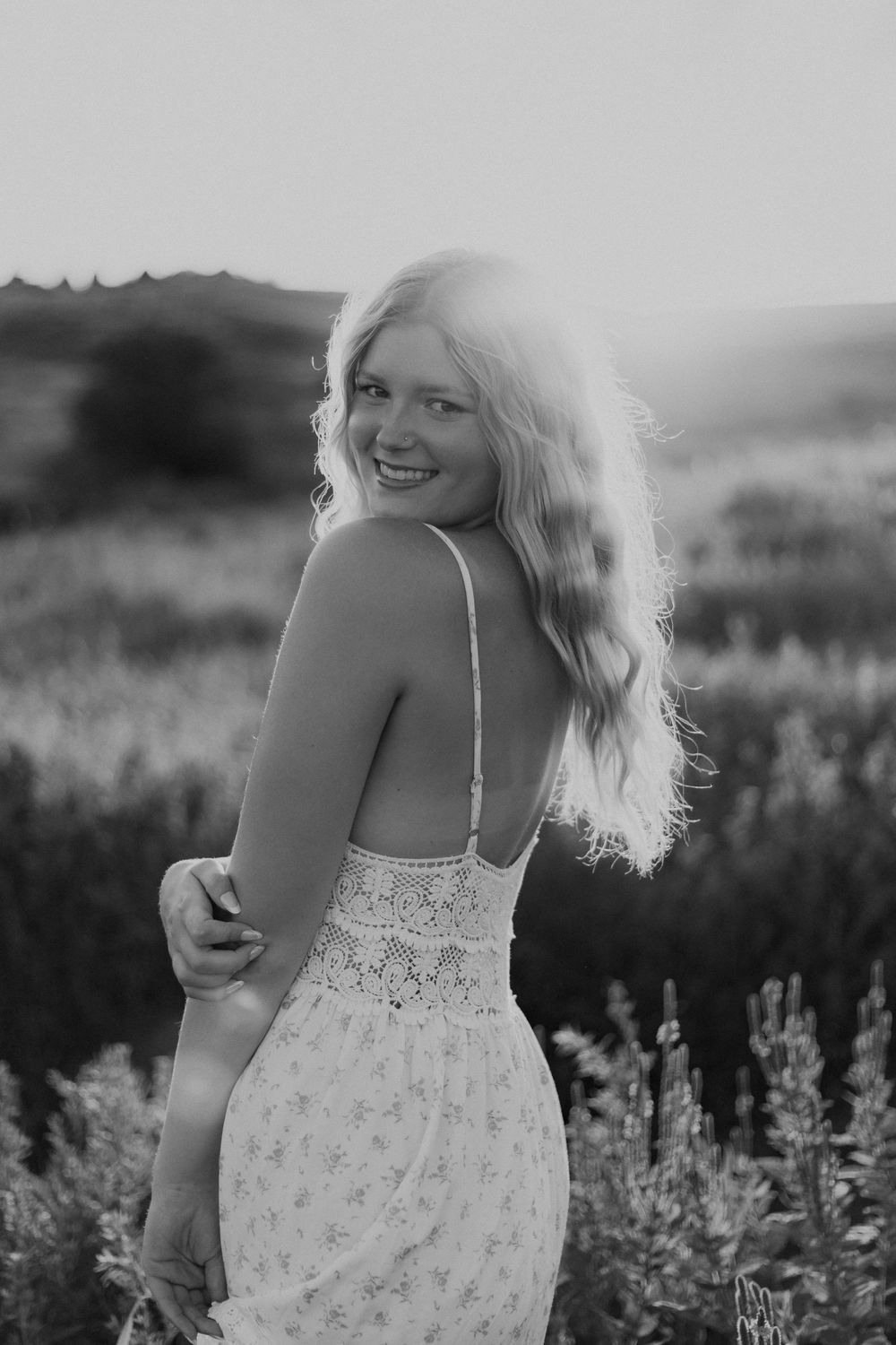 Woman in white floral dress stands among wildflowers in black and white outdoor portrait series.
