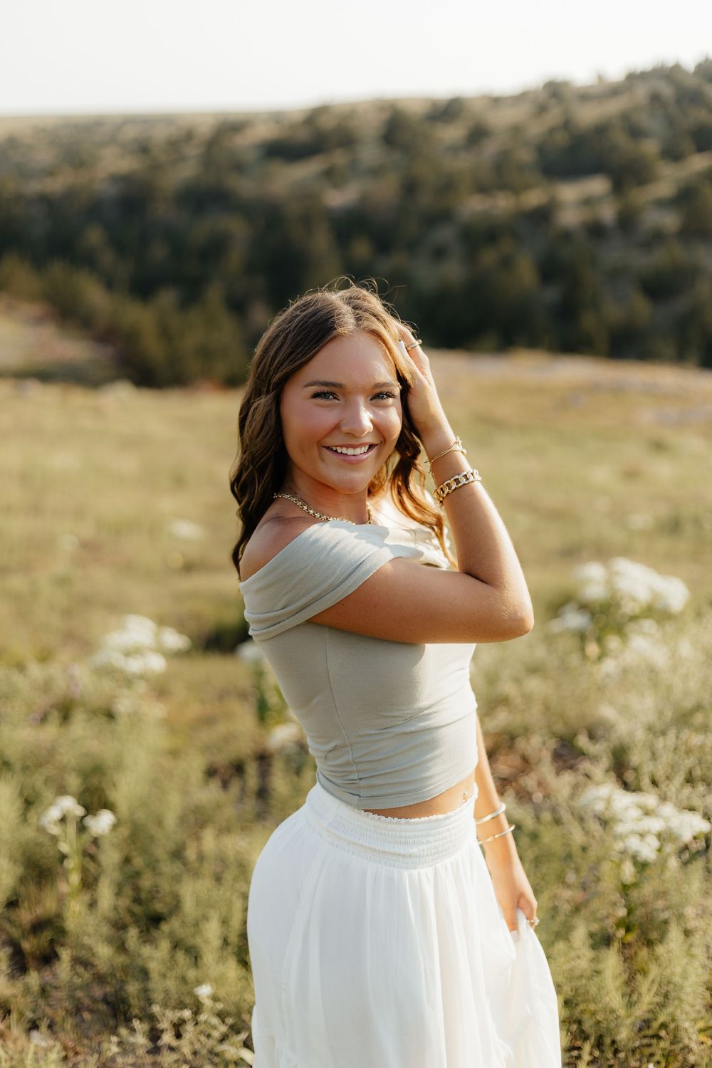 A person in a white dress poses gracefully in a sunlit meadow with wildflowers during golden hour.