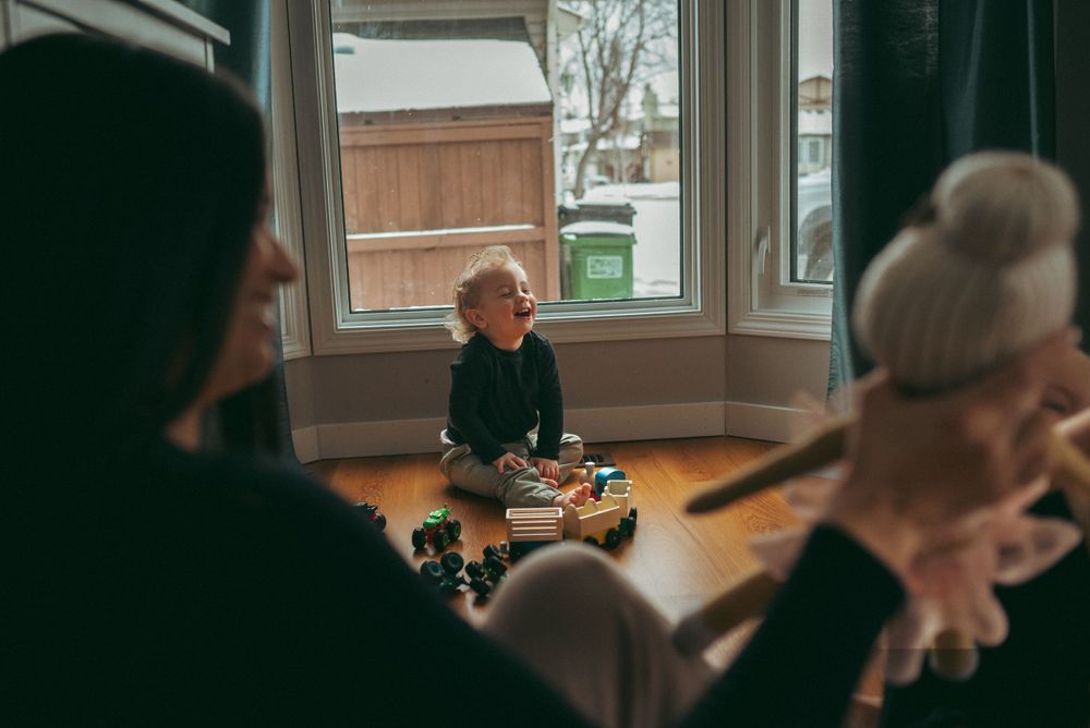 People gather around a sunny window bay in a living room space during a casual indoor meeting.