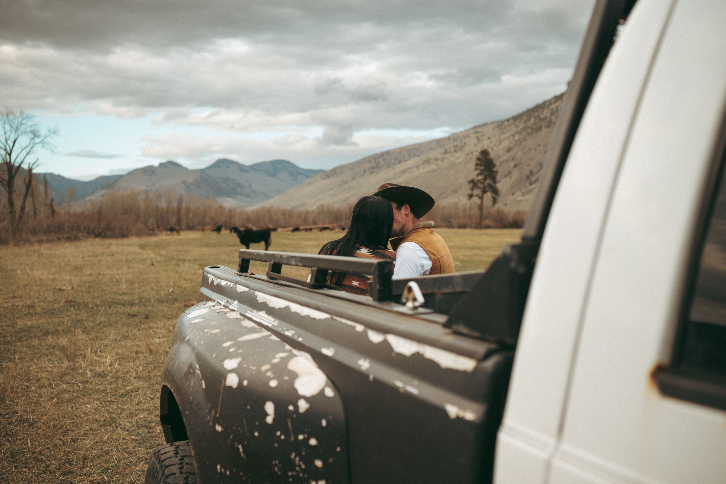 Someone lies on top of a white van's roof photographing a scenic mountain landscape under moody clouds.