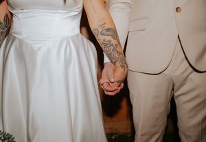 Close-up of a couple holding hands at their wedding, with bride in white dress and groom in beige suit.