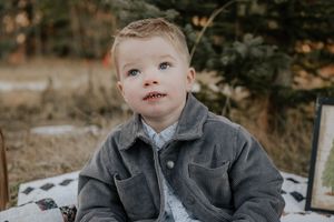 A young child wearing a gray jacket poses outdoors during a fall photoshoot in a natural setting.