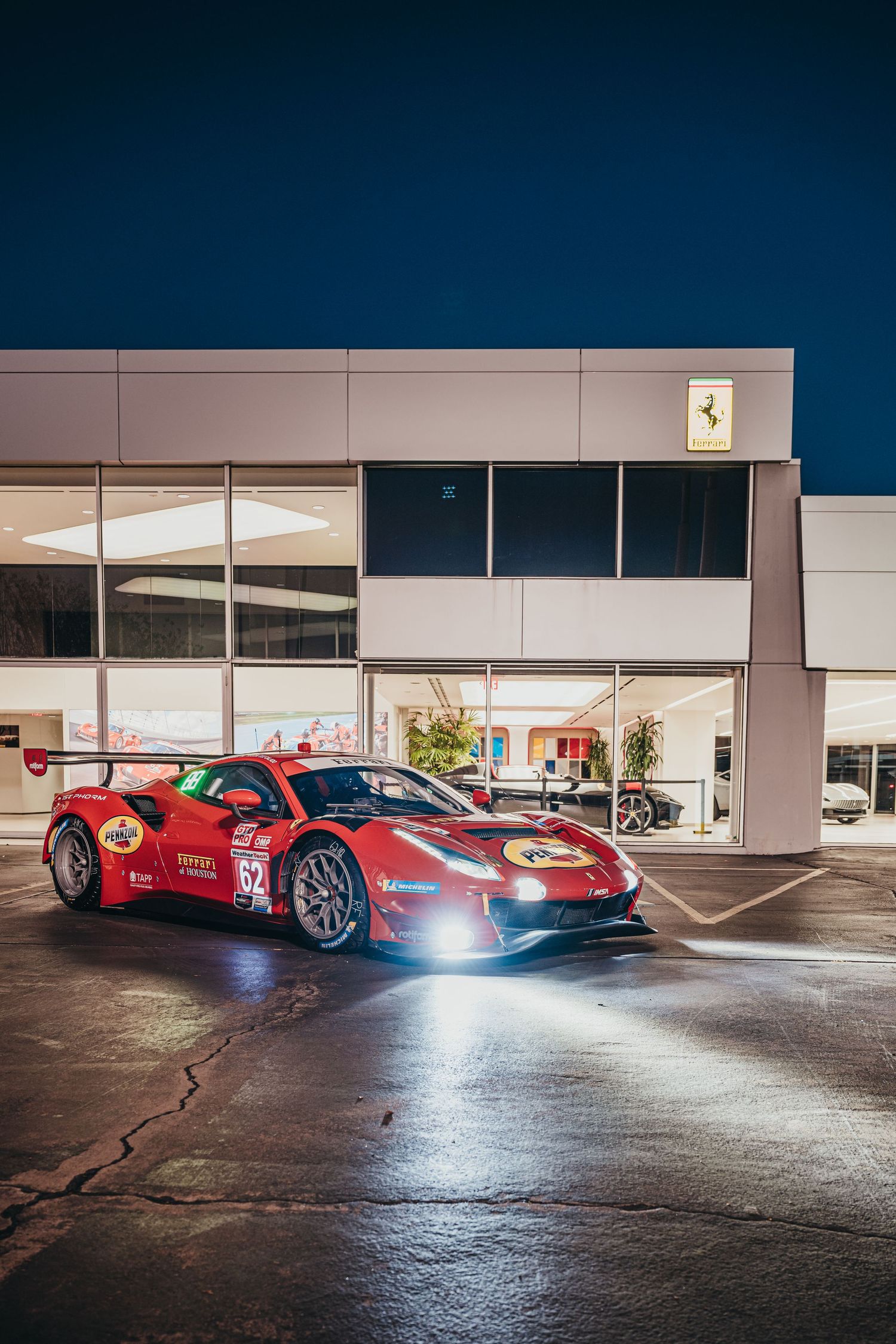 Red Ferrari race cars parked outside modern building at night with dramatic lighting.