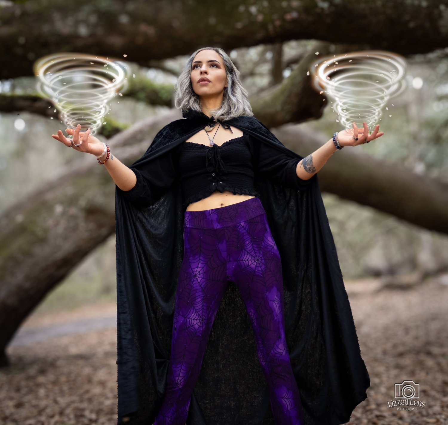 Woman in black cape and purple leggings poses with glowing tornado effects in her hands.