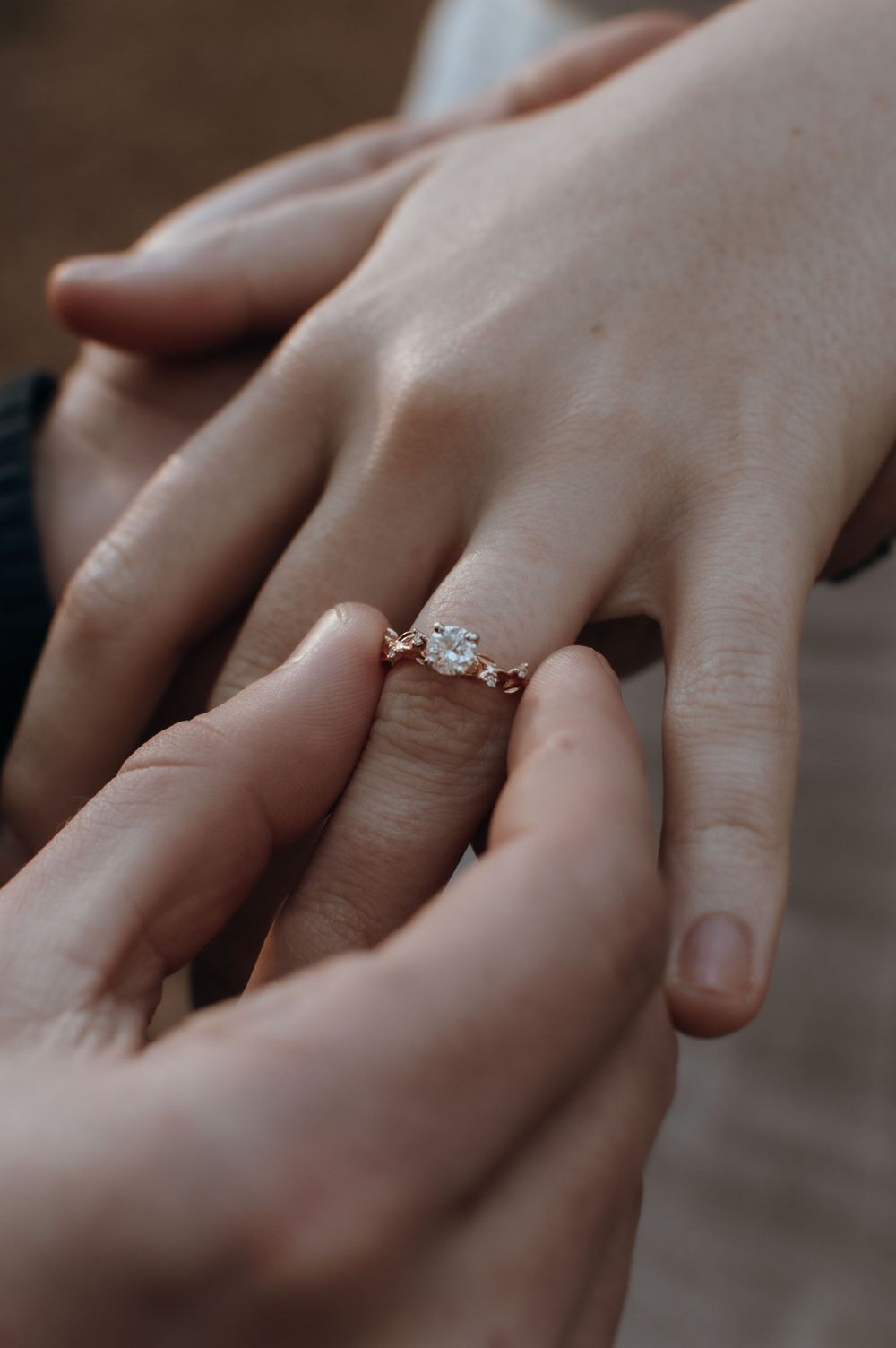 Close-up of hands placing a delicate engagement ring during a proposal moment.