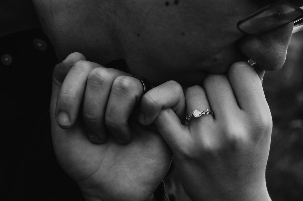 Black and white close-up of two hands making a pinky promise with an engagement ring.