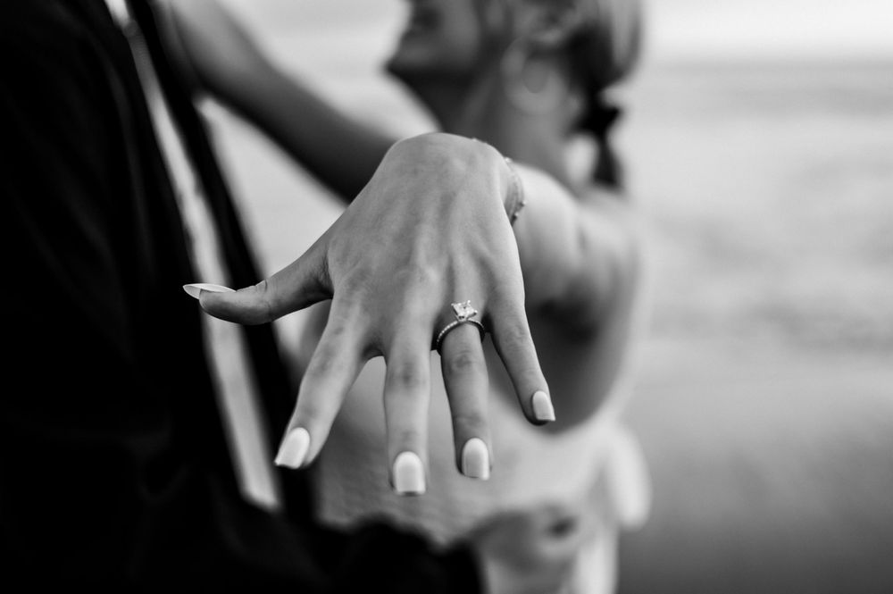 Black and white close-up of hand displaying engagement ring against blurred background.