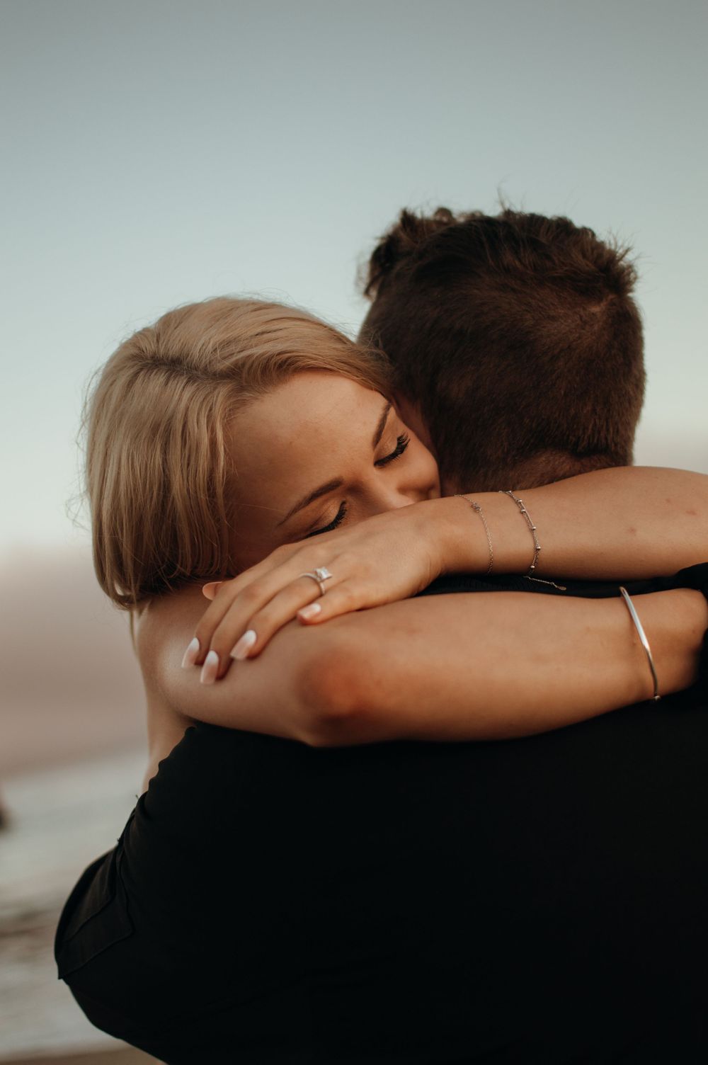 Close-up of couple embracing with engagement ring visible on hand.
