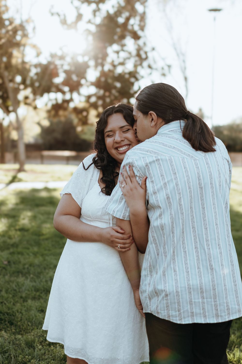 A couple shares a tender embrace during their engagement photoshoot in a park.