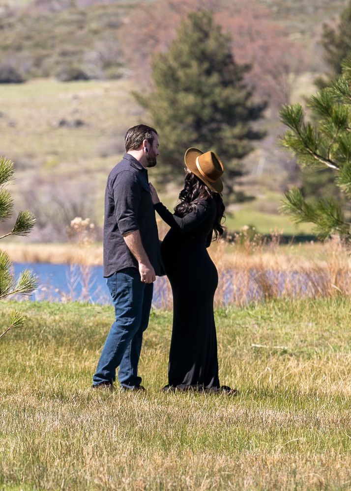 Outdoor maternity photo at Lake Cuyamaca with mom in black dress and dad holding her belly. San Diego maternity photographer