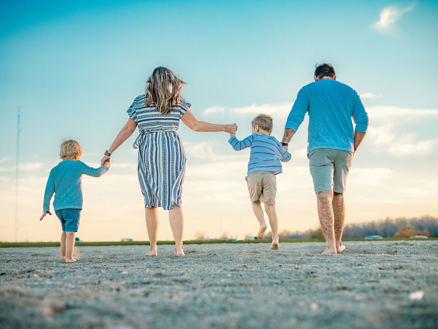 Family holding hands while walking together on a beach during golden hour.
