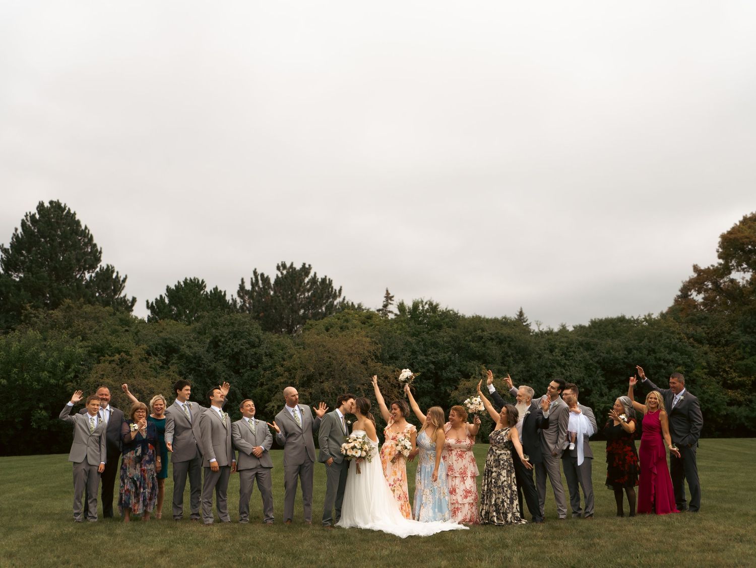 Wedding party celebrating on a lawn with raised arms and cheers.