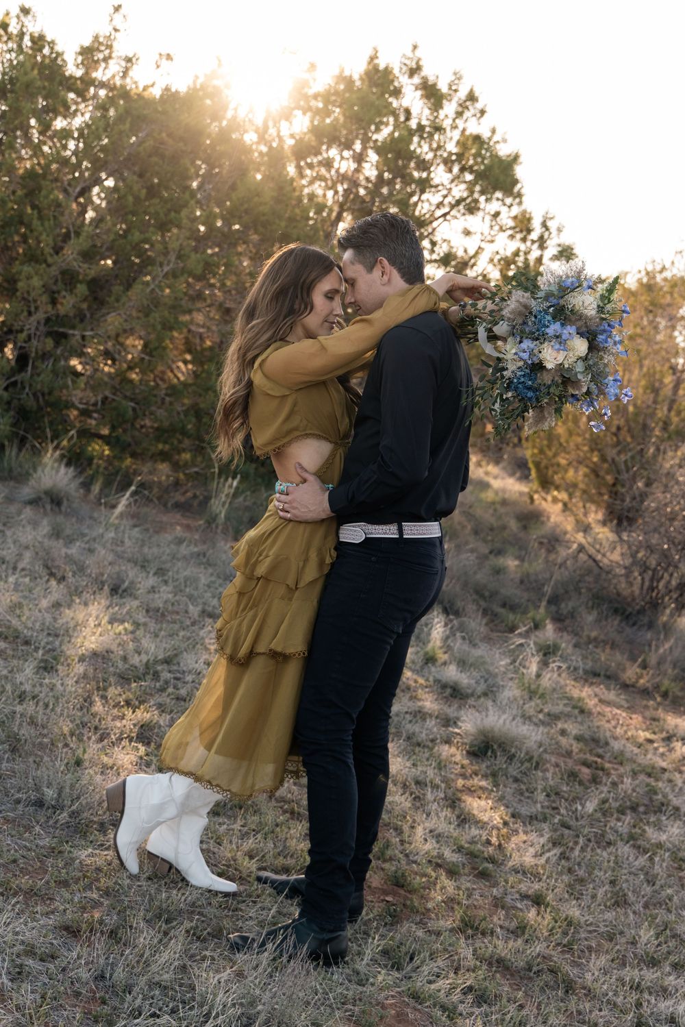 A couple embraces in a tender moment at sunset on a hillside while wearing romantic fall outfits.