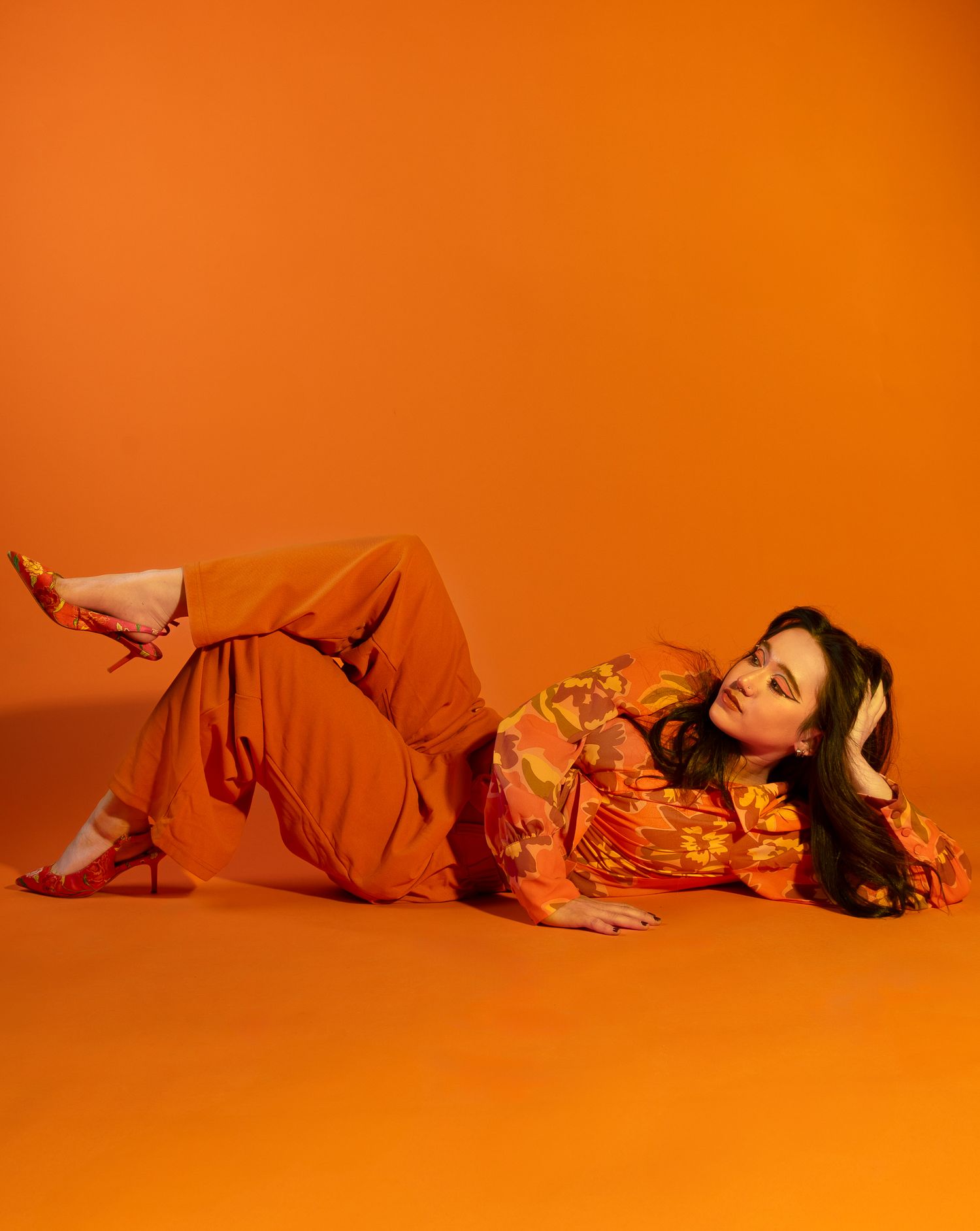 Girl posing in all orange and orange backdrop, legs crossed to the side