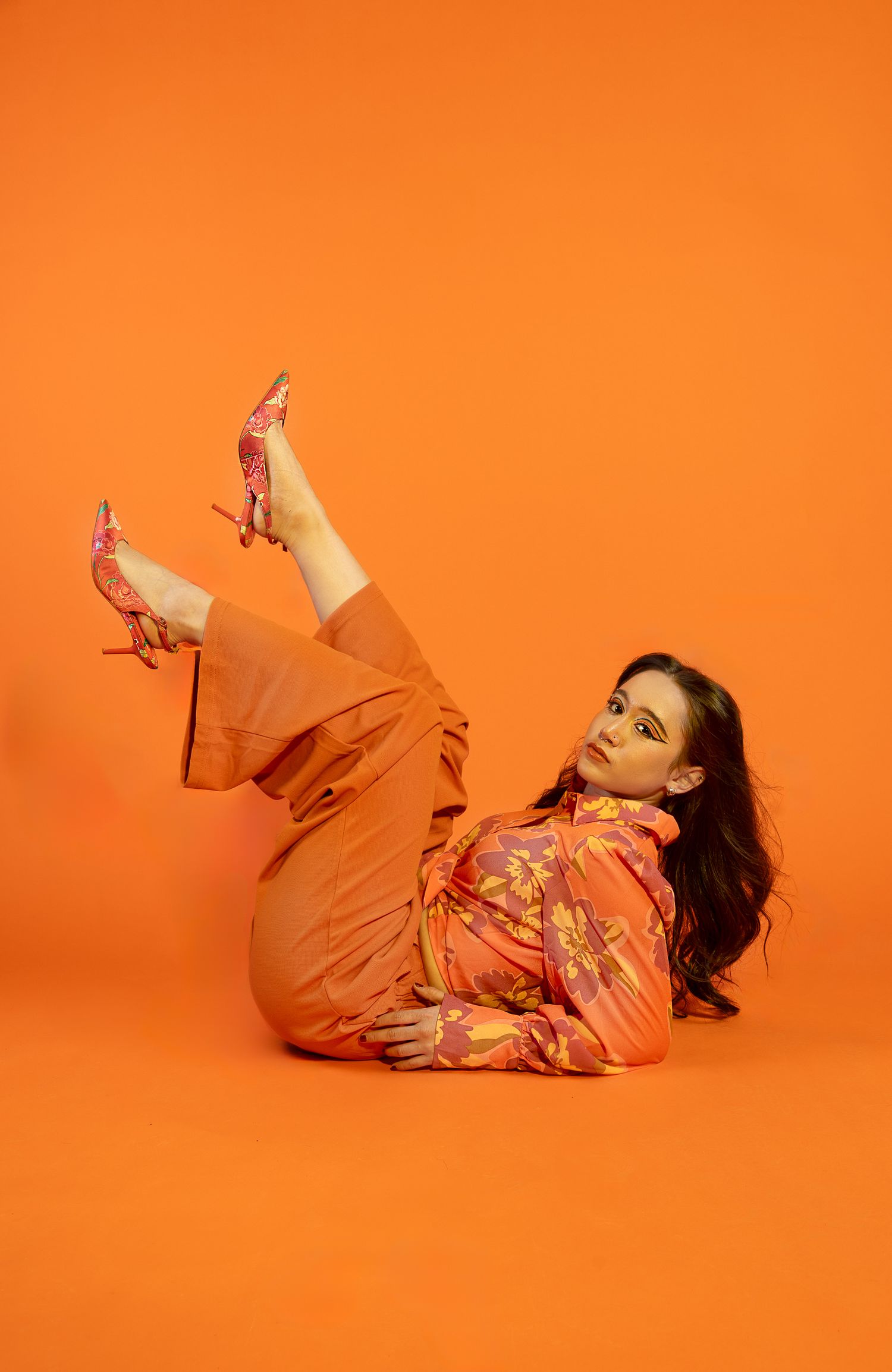 Girl posing in all orange and orange backdrop, legs in the air with eyes open